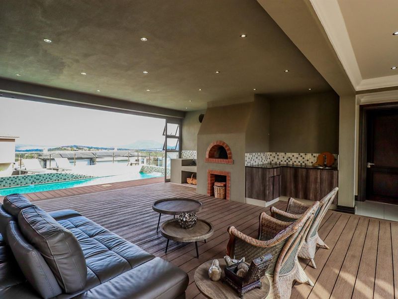 Spacious covered patio featuring timber decking, a built-in pizza oven, braai area, and integrated cabinetry, overlooking a private swimming pool with scenic views.
