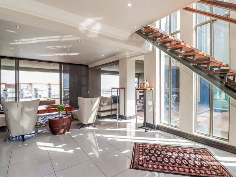 Spacious, modern living area featuring polished tiled floors, a striking floating staircase with glass balustrades, and large windows providing abundant natural light.