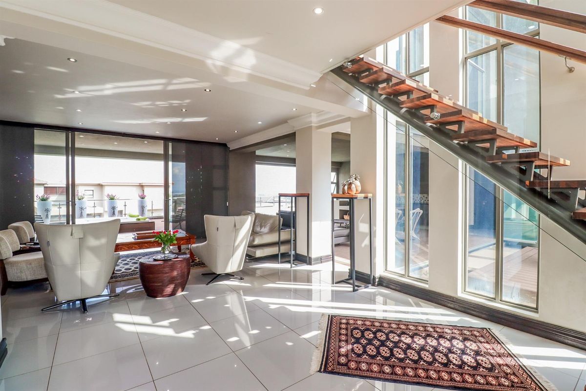 Spacious, modern living area featuring polished tiled floors, a striking floating staircase with glass balustrades, and large windows providing abundant natural light.