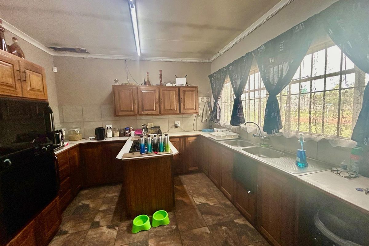 A dated kitchen featuring wooden cabinetry, tiled flooring, and a double sink, requiring cosmetic updates to modernize the space.