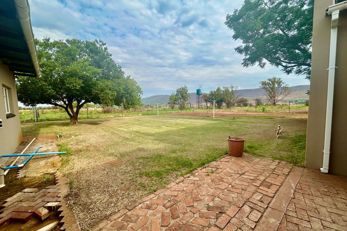 Spacious rear garden featuring a brick-paved patio area, established trees, and open views of the surrounding farm landscape.
