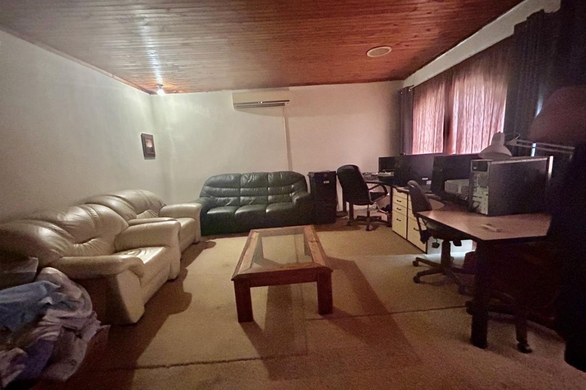 A spacious living area featuring a timber-clad ceiling, wall-mounted air conditioning unit, and carpeted flooring, suitable for a multi-purpose lounge or home office space.