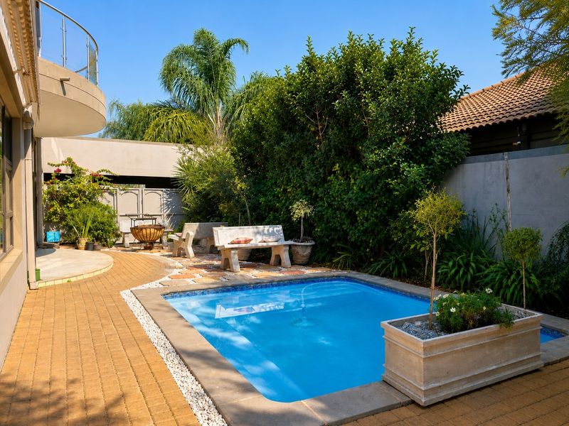A well-maintained outdoor pool area featuring a paved patio, landscaped garden, and a balcony overlooking the private backyard space.