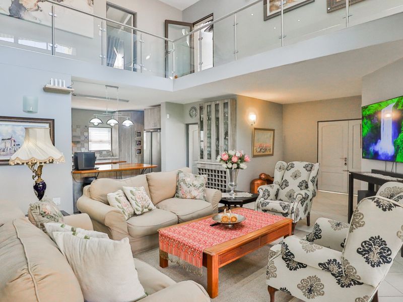 Spacious open-plan living area featuring a double-volume ceiling, glass mezzanine balustrade, and an integrated kitchen with a breakfast island.