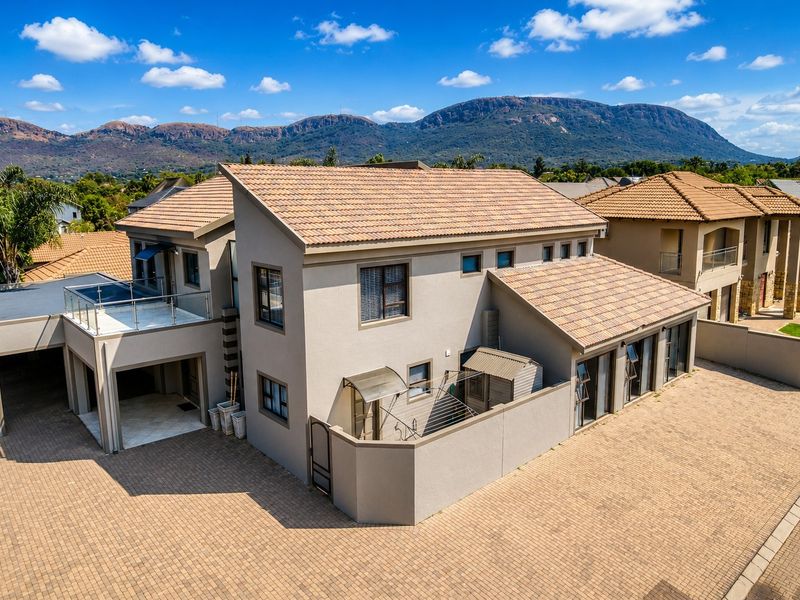 Aerial view of a modern double-story residential property featuring a tiled roof, paved driveway, and an upper-level balcony with mountain views.