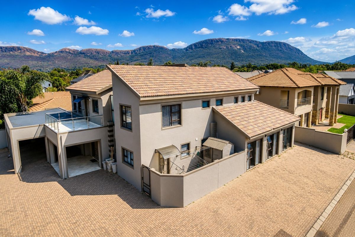 Aerial view of a modern double-story residential property featuring a tiled roof, paved driveway, and an upper-level balcony with mountain views.