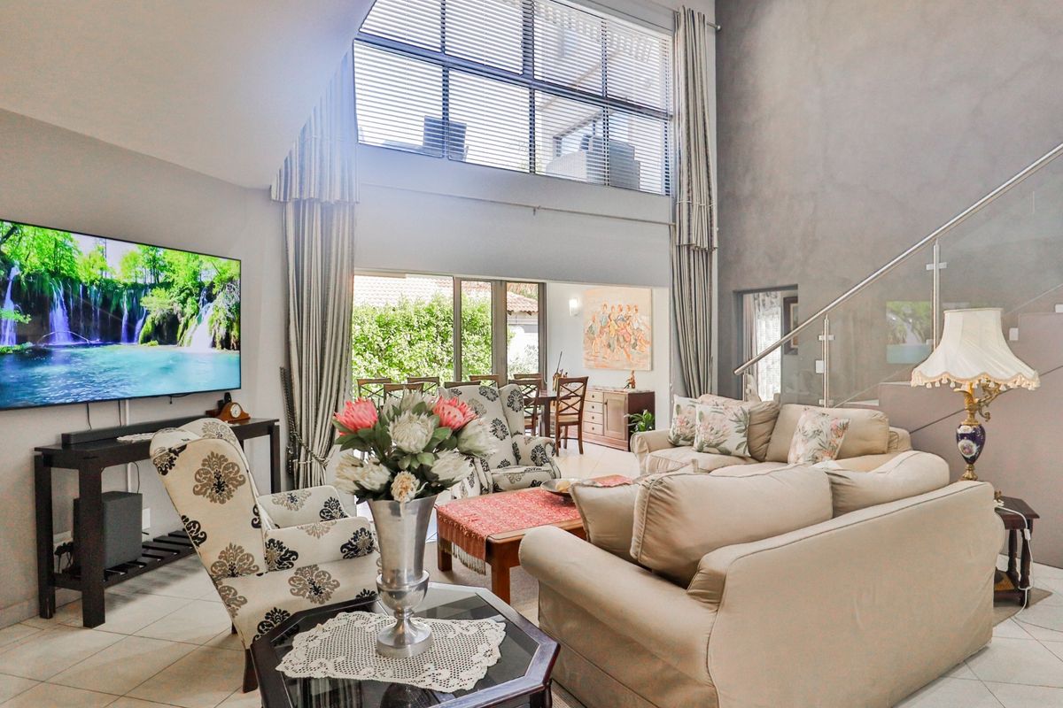 Spacious double-volume living room featuring large windows, tiled flooring, and a modern glass balustrade staircase leading to the upper level.