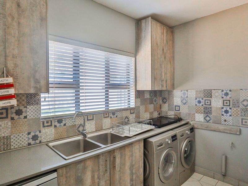 A well-appointed laundry room featuring modern cabinetry, a double stainless steel sink, patterned tile splashback, and dedicated space for laundry appliances.