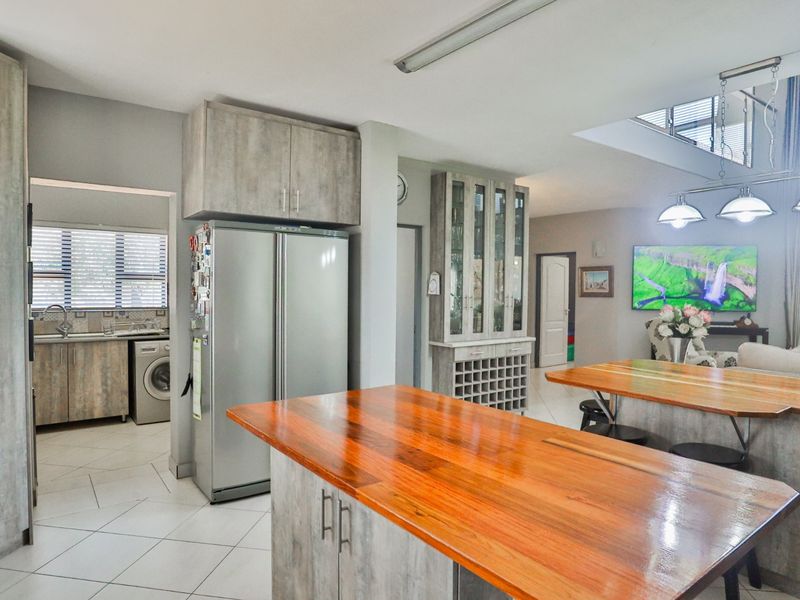 Open plan living area featuring a timber kitchen island, built-in cabinetry with wine storage, and tiled flooring, seamlessly connecting to the adjacent scullery area.