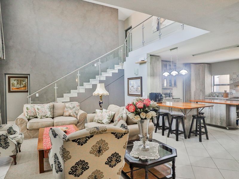 Spacious open-plan living area featuring a modern staircase with glass balustrade, double volume ceilings, and a well-appointed kitchen with a central island.