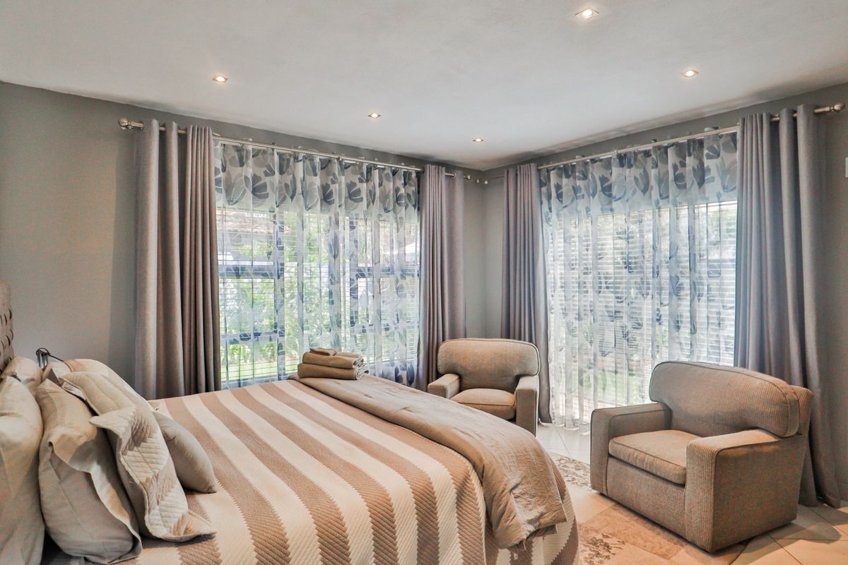 A well-maintained bedroom featuring tiled flooring, recessed downlights, and large windows with curtain tracks, offering a bright and comfortable living space.