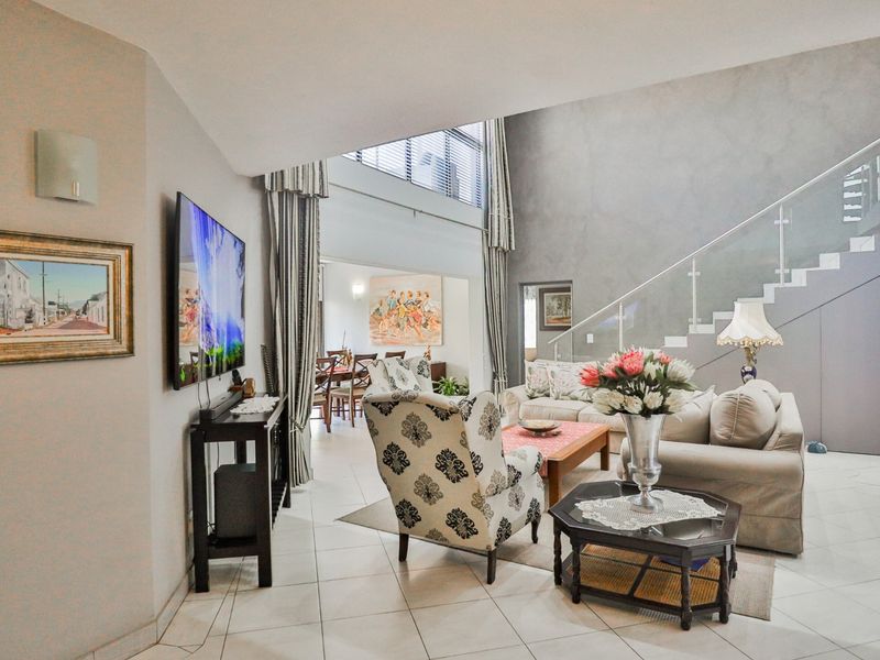Spacious open-plan living area featuring double-volume ceilings, a modern staircase with glass balustrades, and large windows providing ample natural light.