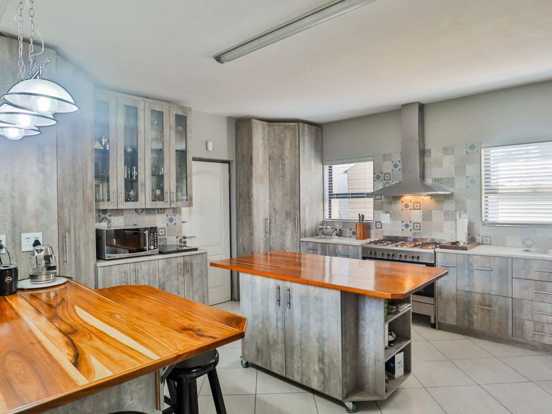 Modern kitchen featuring wood-look cabinetry, a central wooden island, gas stove with extractor fan, and decorative tiled backsplash.