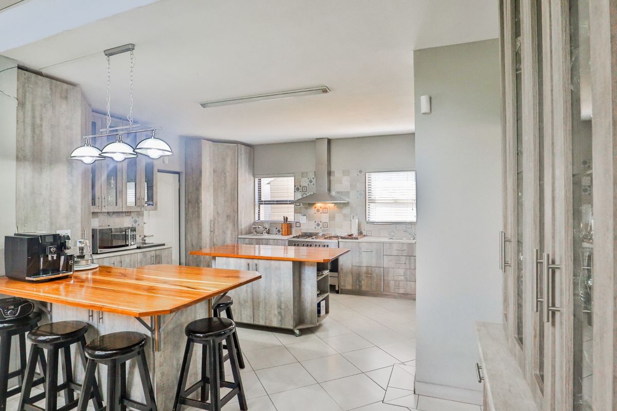 Spacious kitchen featuring a large wooden island, modern cabinetry, gas hob with extractor fan, and tiled flooring in an open-plan layout.