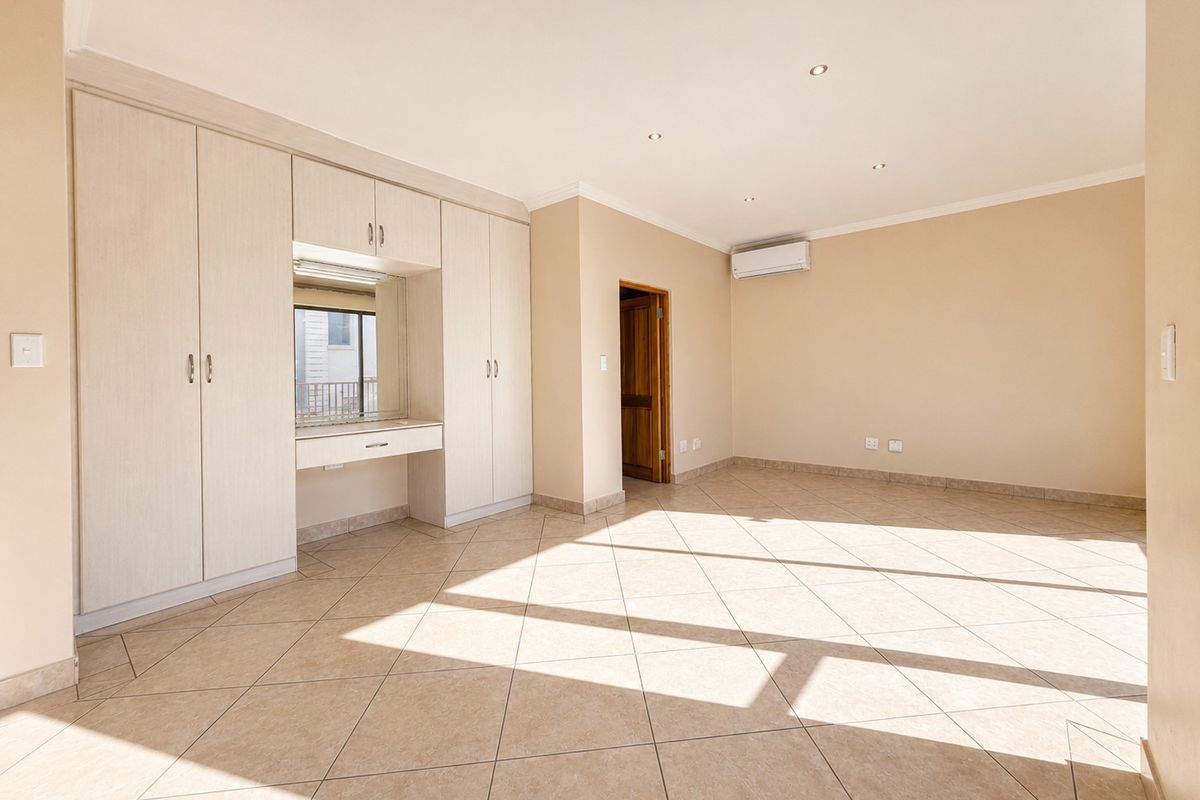 Spacious bedroom featuring built-in cupboards with a vanity area, tiled flooring, recessed ceiling lighting, and a wall-mounted air conditioning unit.