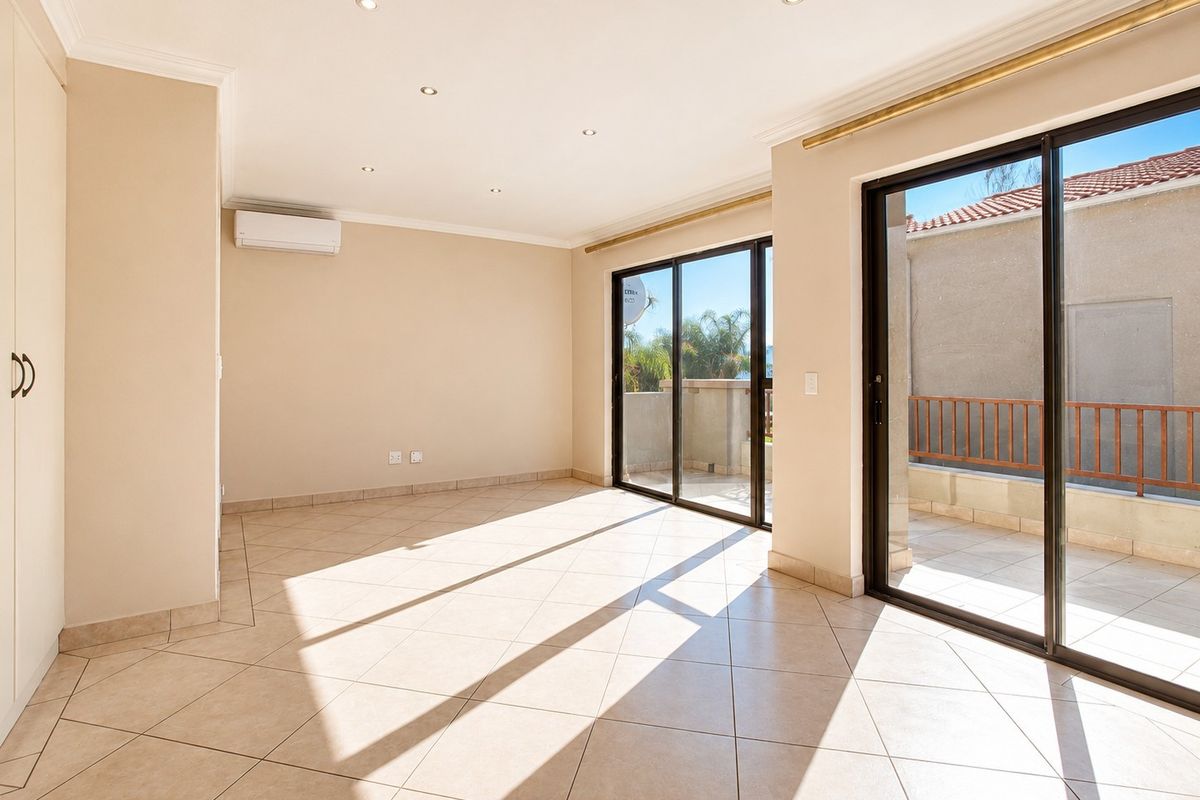 Bright and spacious living area featuring neutral floor tiles, recessed downlighting, a wall-mounted air conditioning unit, and large sliding glass doors leading to a balcony.