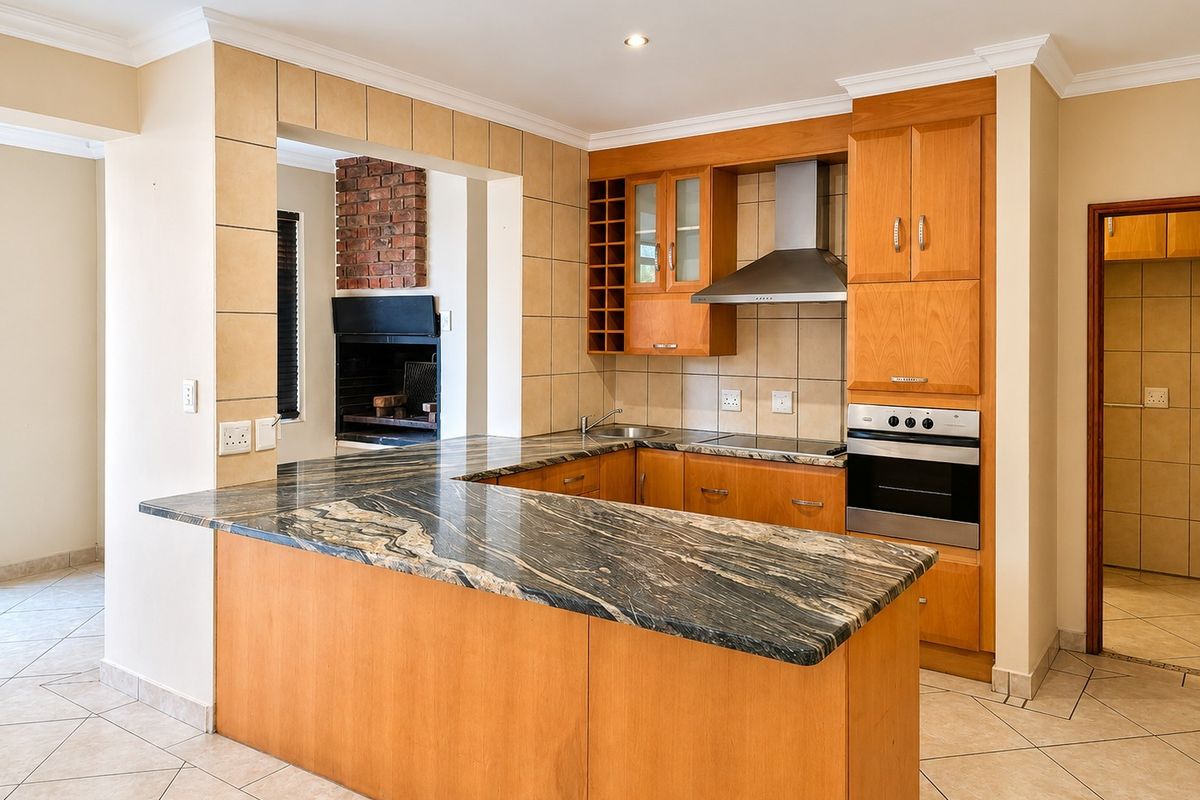 Functional kitchen featuring wooden cabinetry, granite countertops, built-in oven, extractor fan, and an integrated indoor braai area.