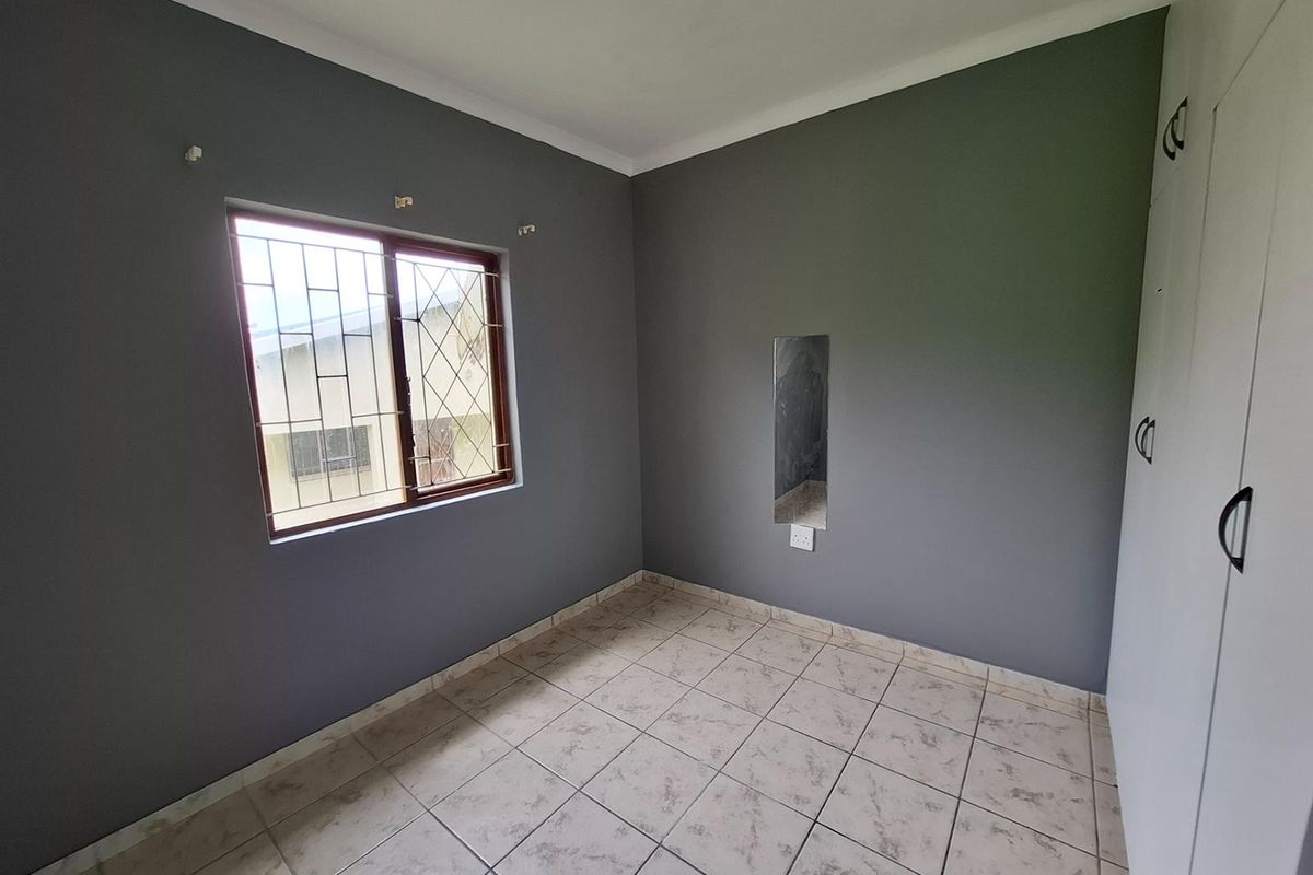 A neutral-toned bedroom featuring tiled flooring, built-in cupboards, and a window with security bars.
