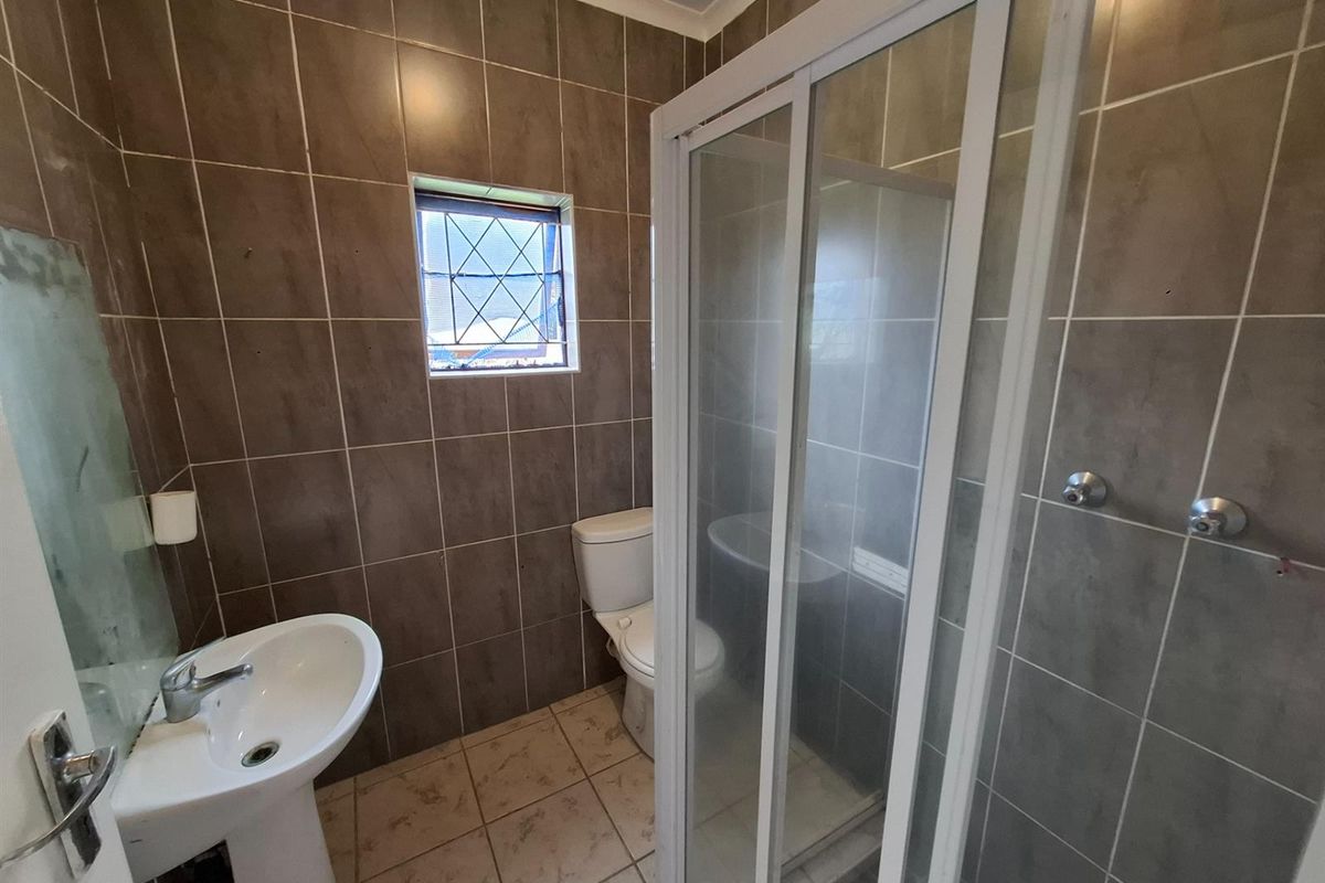 A functional bathroom featuring a pedestal basin, a toilet, and a glass-enclosed shower with full-height wall tiling.