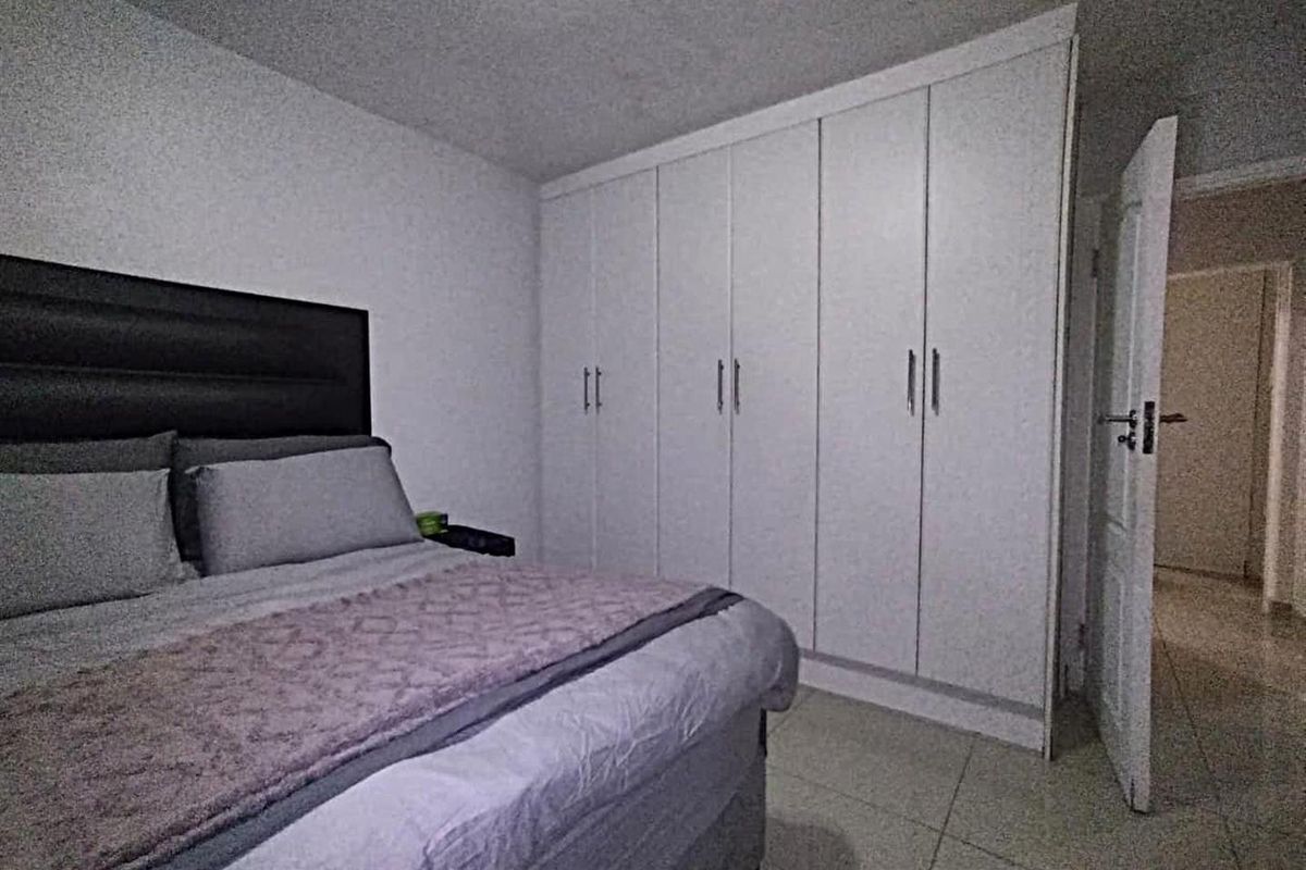 A well-maintained bedroom featuring neutral tiled flooring and ample built-in cupboard storage space.