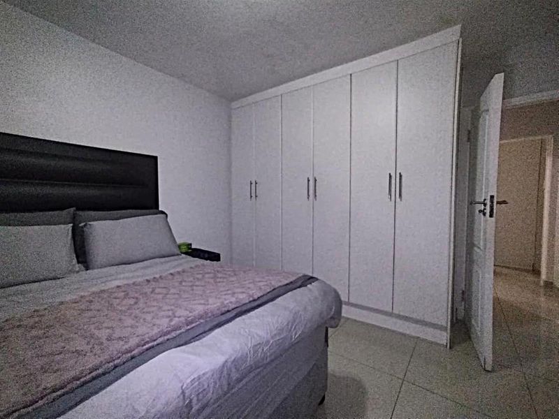 A well-maintained bedroom featuring neutral tiled flooring and ample built-in cupboard storage space.