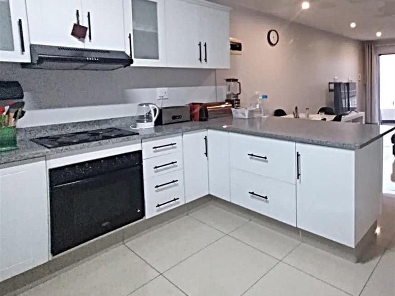 Modern open-plan kitchen featuring white cabinetry, granite countertops, built-in oven, gas hob, and tiled flooring, seamlessly flowing into the adjacent living area.