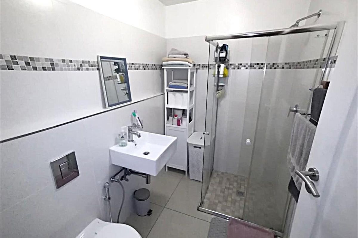 A modern bathroom featuring a wall-mounted basin, a glass-enclosed shower, and a wall-mounted toilet with a concealed cistern.