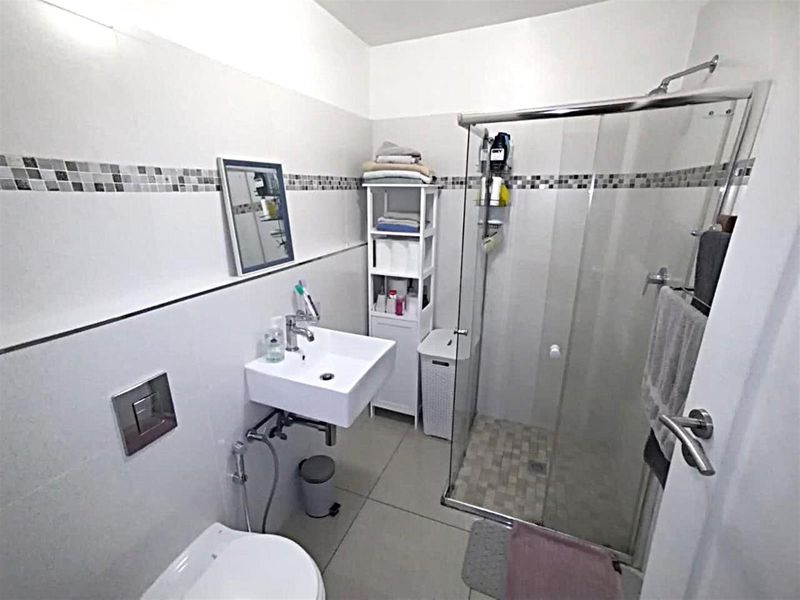 A modern bathroom featuring a wall-mounted basin, a glass-enclosed shower, and a wall-mounted toilet with a concealed cistern.