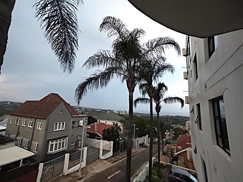 An elevated view overlooking the surrounding neighbourhood, street, and distant coastline from an apartment balcony.