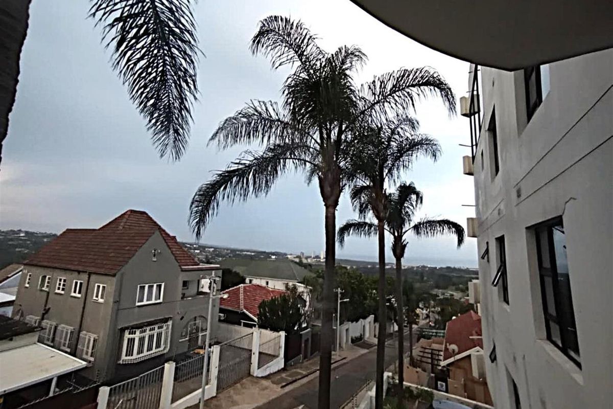 An elevated view overlooking the surrounding neighbourhood, street, and distant coastline from an apartment balcony.