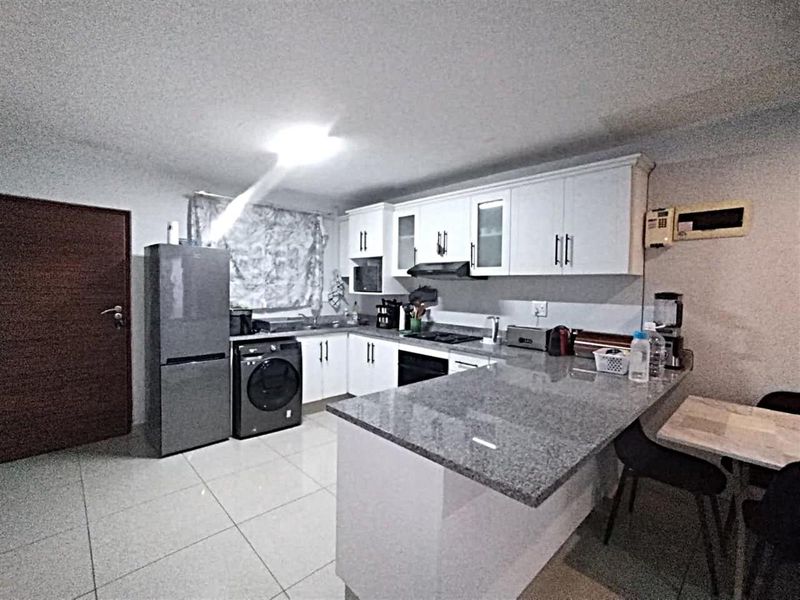 Modern kitchen featuring granite countertops, white cabinetry, built-in oven, hob, extractor fan, and tiled flooring with an integrated breakfast bar area.