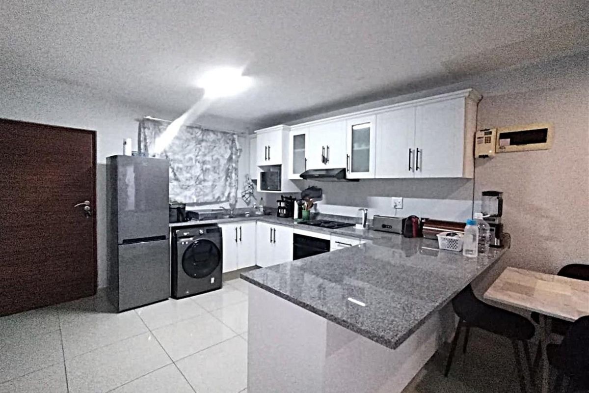 Modern kitchen featuring granite countertops, white cabinetry, built-in oven, hob, extractor fan, and tiled flooring with an integrated breakfast bar area.