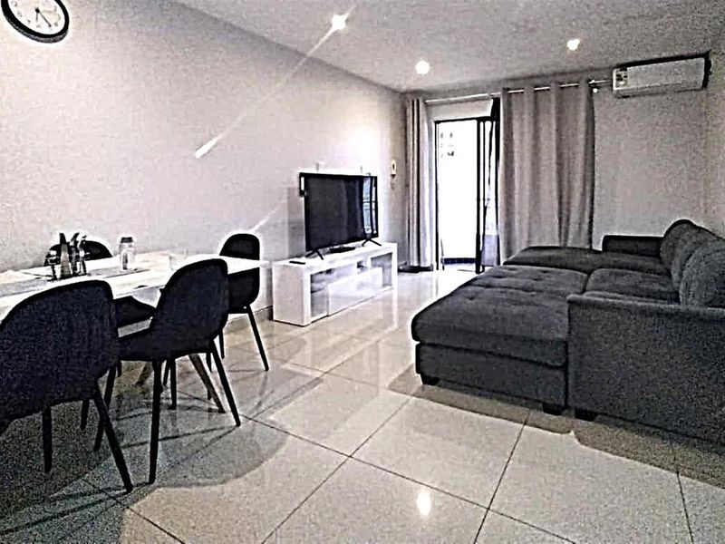 Open-plan living and dining area featuring polished tiled flooring, recessed lighting, and a wall-mounted air conditioning unit with access to an outdoor space.