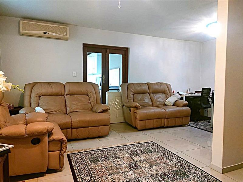 A spacious living room featuring tiled flooring, a wall-mounted split-system air conditioner, and access to an adjoining area through double glass doors.