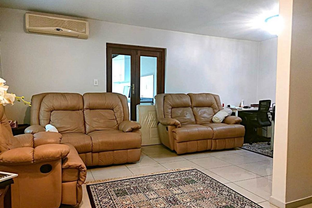 A spacious living room featuring tiled flooring, a wall-mounted split-system air conditioner, and access to an adjoining area through double glass doors.