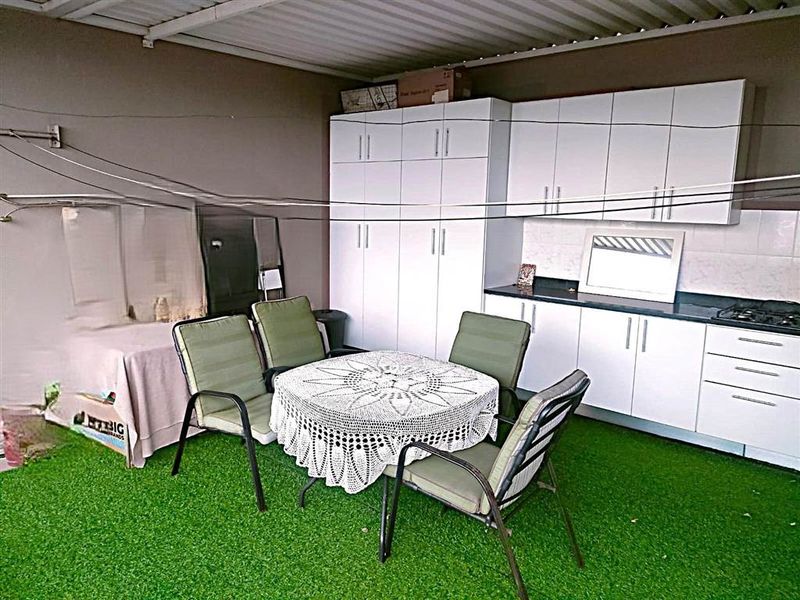 Covered patio area featuring built-in cabinetry, a gas hob, and artificial grass flooring, providing a functional outdoor entertainment and prep space.