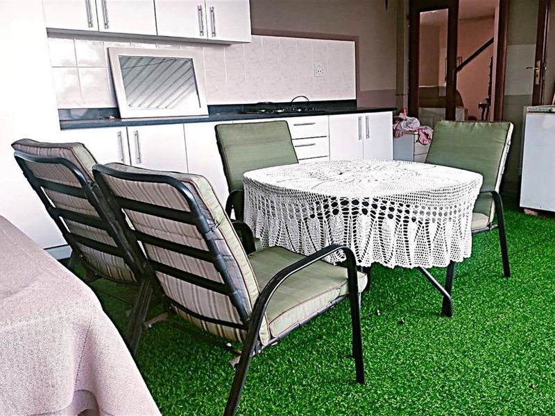 Covered patio area featuring built-in cabinetry, a hob, and artificial grass flooring, providing a functional outdoor entertainment space.