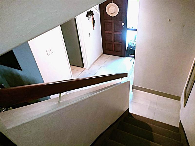 A view looking down a staircase towards the tiled entryway, featuring a solid timber front door and a wooden handrail.