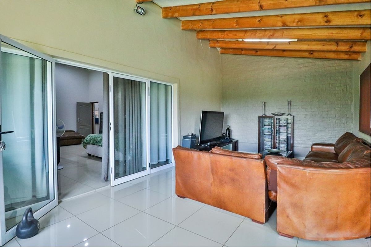 Living area featuring exposed timber ceiling beams, tiled flooring, and sliding glass doors providing access to an adjacent bedroom.