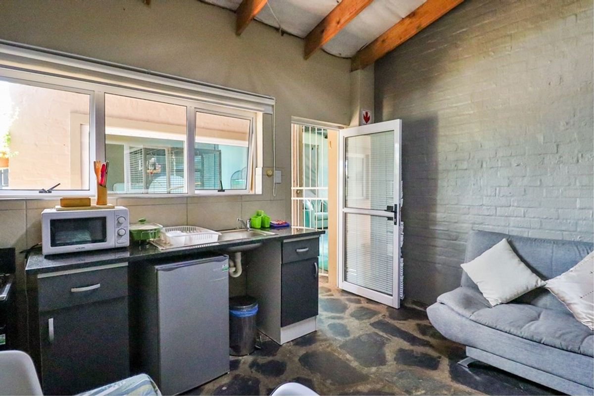 Compact kitchen area featuring dark cabinetry, granite countertops, stone flooring, and exposed timber beams, with direct access to an exterior security gate.