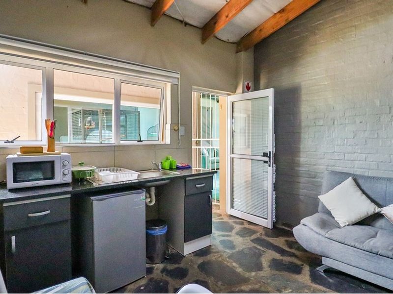 Compact kitchen area featuring dark cabinetry, granite countertops, stone flooring, and exposed timber beams, with direct access to an exterior security gate.