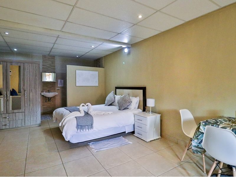 Spacious bedroom featuring tiled flooring, a drop ceiling with recessed lighting, and an integrated wash basin area with a built-in wardrobe.
