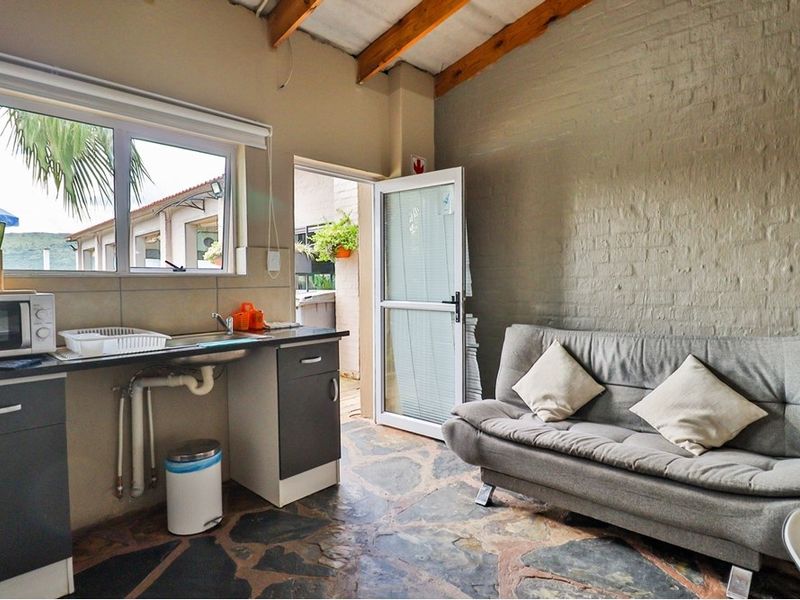 Open-plan kitchenette and living area featuring exposed timber rafters, stone flooring, and an exposed brick wall with direct access to an outdoor area.