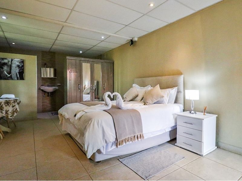 A spacious bedroom featuring tiled flooring, a drop ceiling with recessed lighting, a built-in wardrobe, and an integrated vanity basin area.