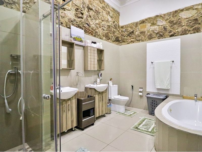 Spacious bathroom featuring a double vanity, glass-enclosed shower, built-in bathtub, and a distinctive stone feature wall with neutral tiling throughout.