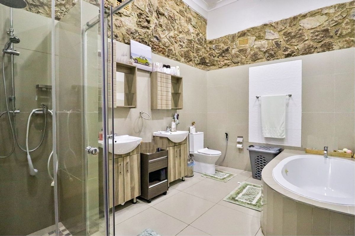 Spacious bathroom featuring a double vanity, glass-enclosed shower, built-in bathtub, and a distinctive stone feature wall with neutral tiling throughout.