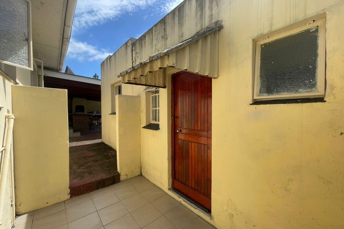 Exterior view of a rear courtyard area featuring a wooden door, tiled flooring, and a metal awning over the entrance.
