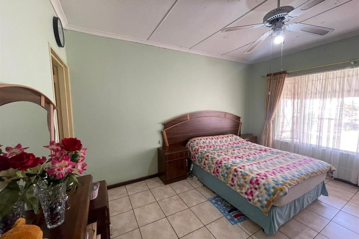 A bedroom featuring tiled flooring, a ceiling fan, and built-in headboard cabinetry, offering a functional space with natural light.