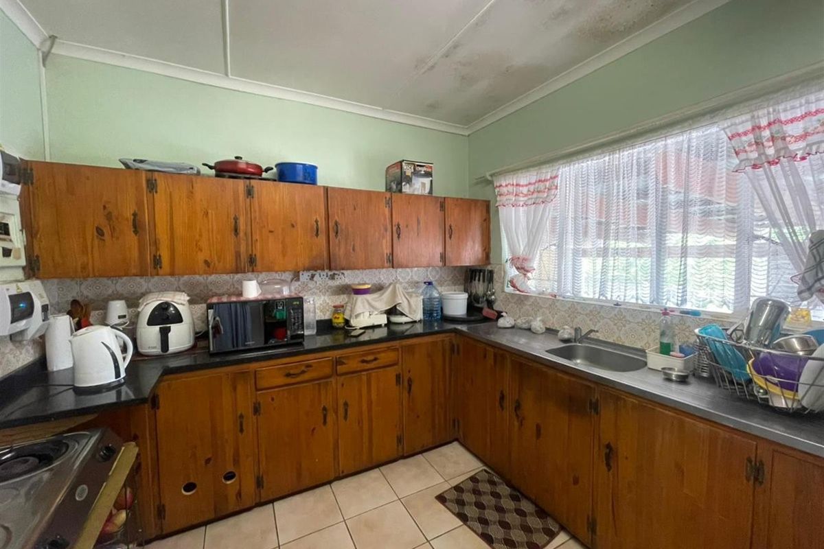 A dated kitchen featuring wooden cabinetry, dark countertops, a stainless steel sink, and tiled flooring, requiring cosmetic updates to modernize the space.
