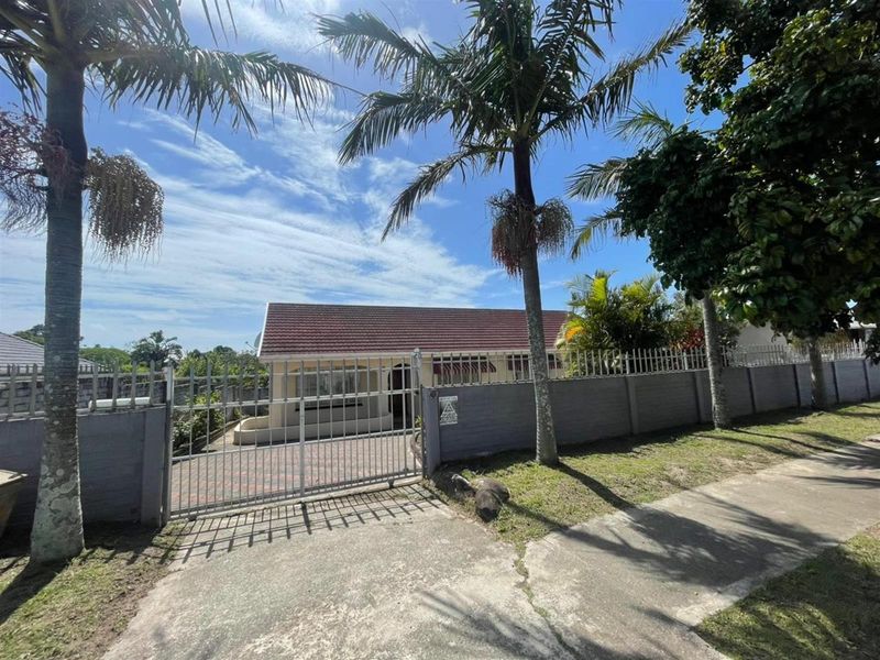 Front view of the property featuring a secure gated entrance, paved driveway, and established palm trees within a fenced perimeter.